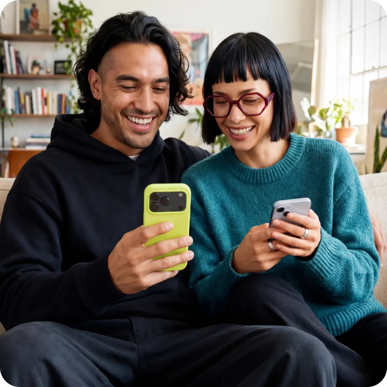 Du žmonės sėdi ant sofos ir žiūrėdami į telefonus šypsosi