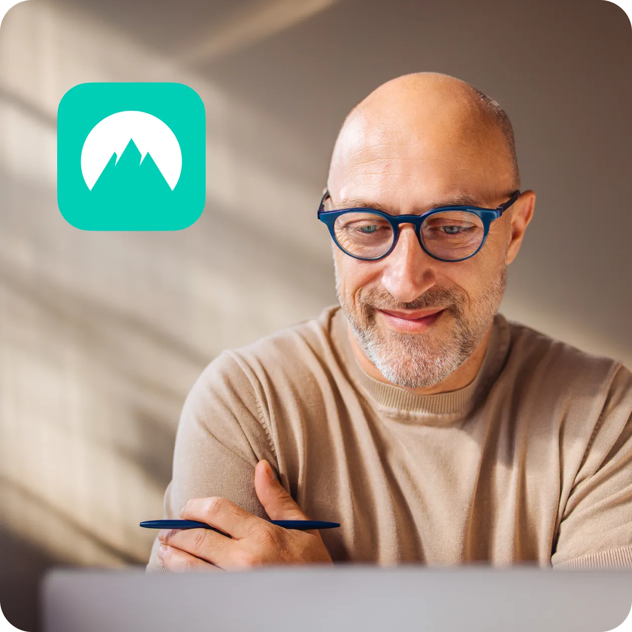 Man with glasses smiling at laptop holding pen 
